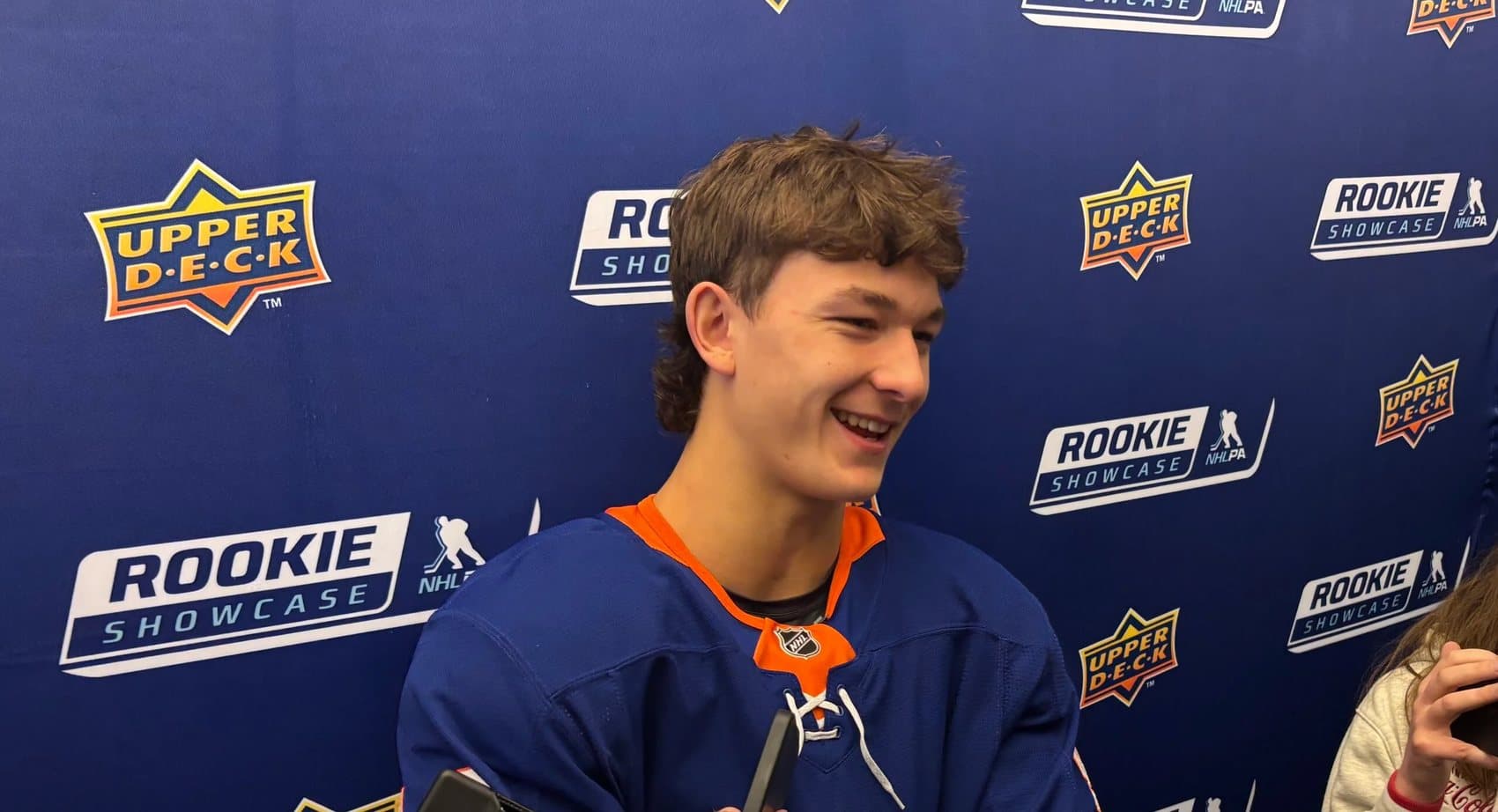 A rookie in a brand-new NHL jersey speaks to reporters in front of a backdrop repeating the Upper Deck and NHLPA Rookie Showcase logos