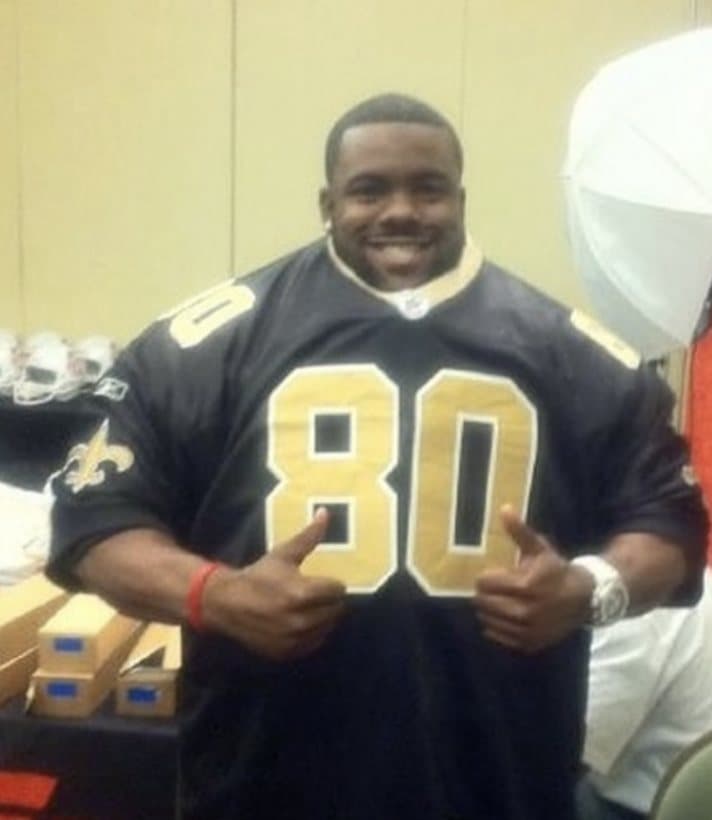 Mark Ingram in a New Orleans Saints number 80 jersey at the 2011 Rookie Premiere, holding the numerals out from his chest, with jersey boxes stacked on a table behind him