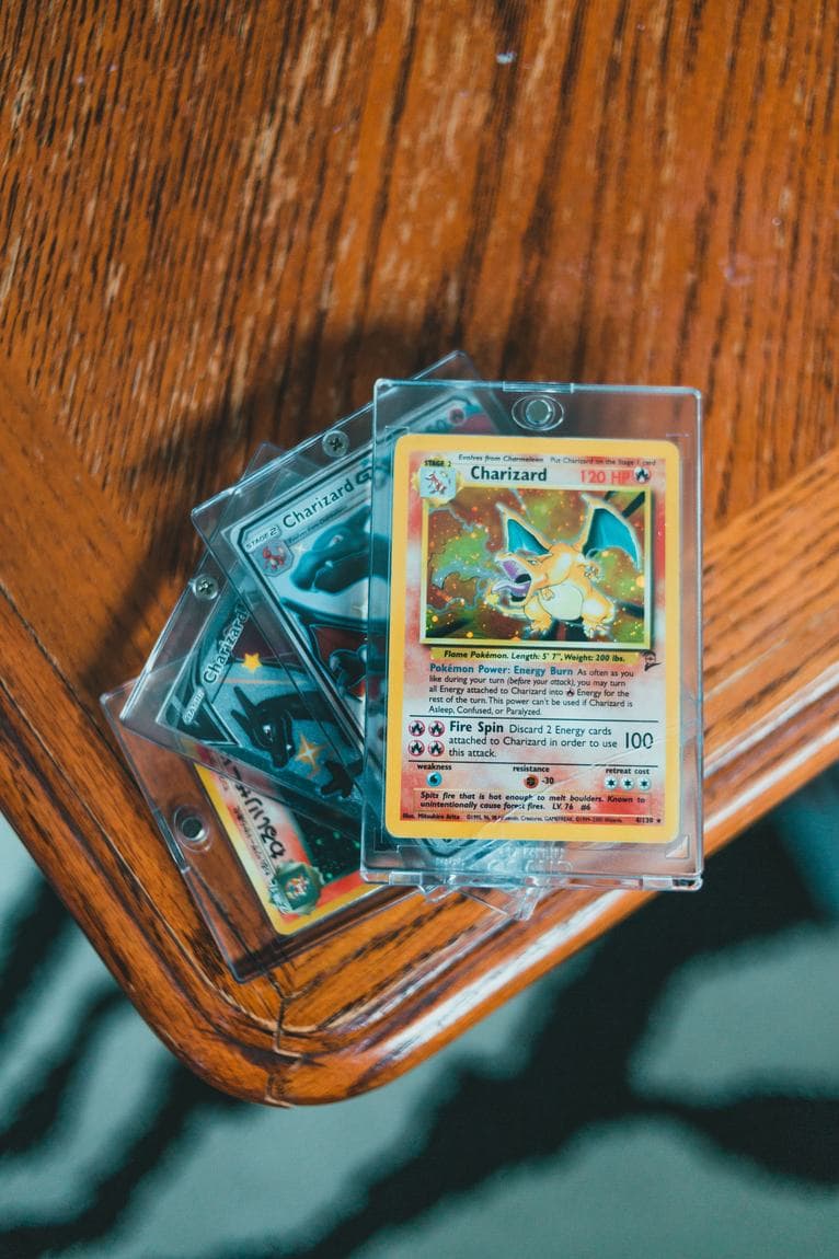 Several Charizard cards in protective toploaders stacked on a wooden table