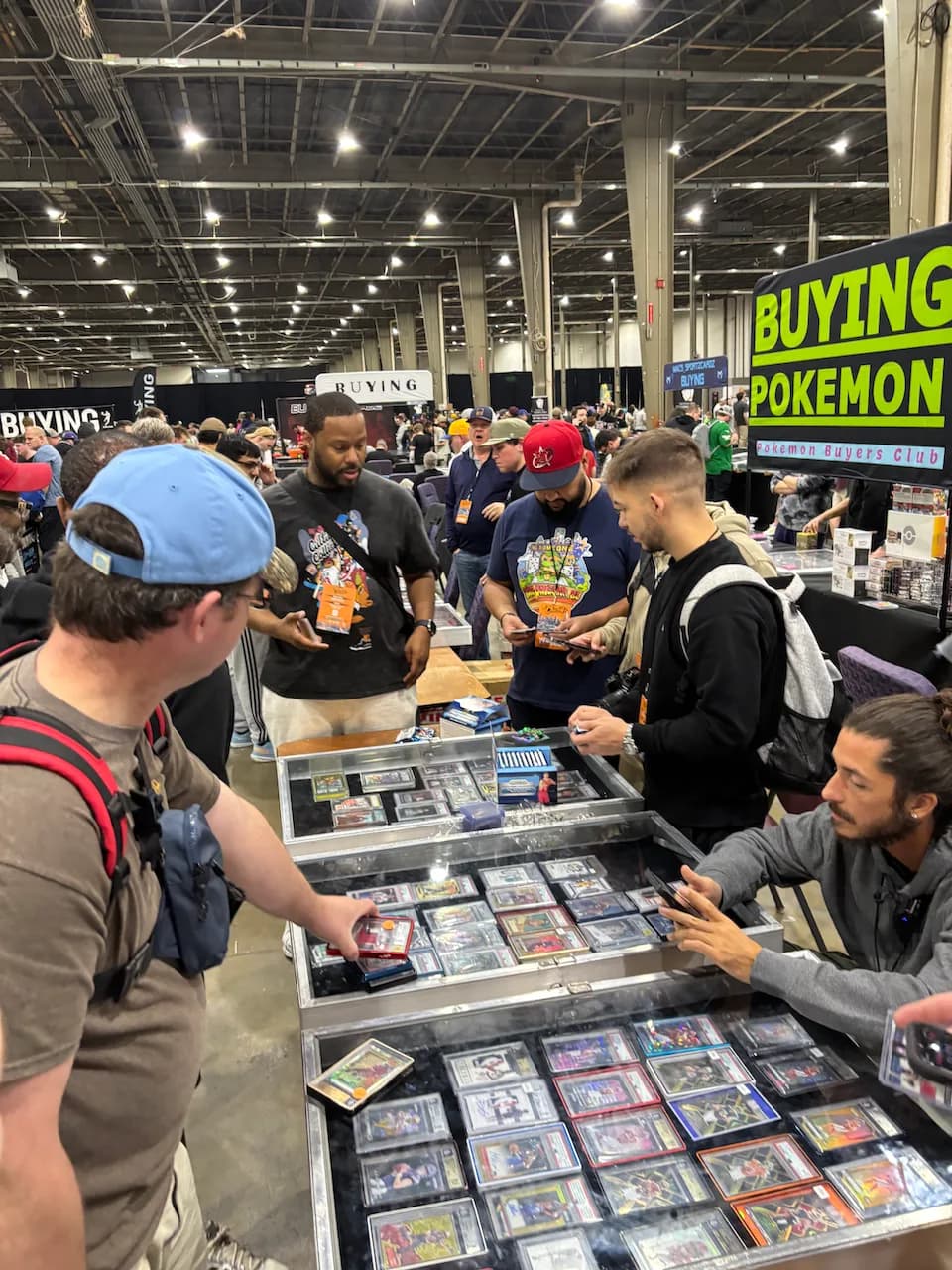 A crowded modern card show floor lined with dealer display cases