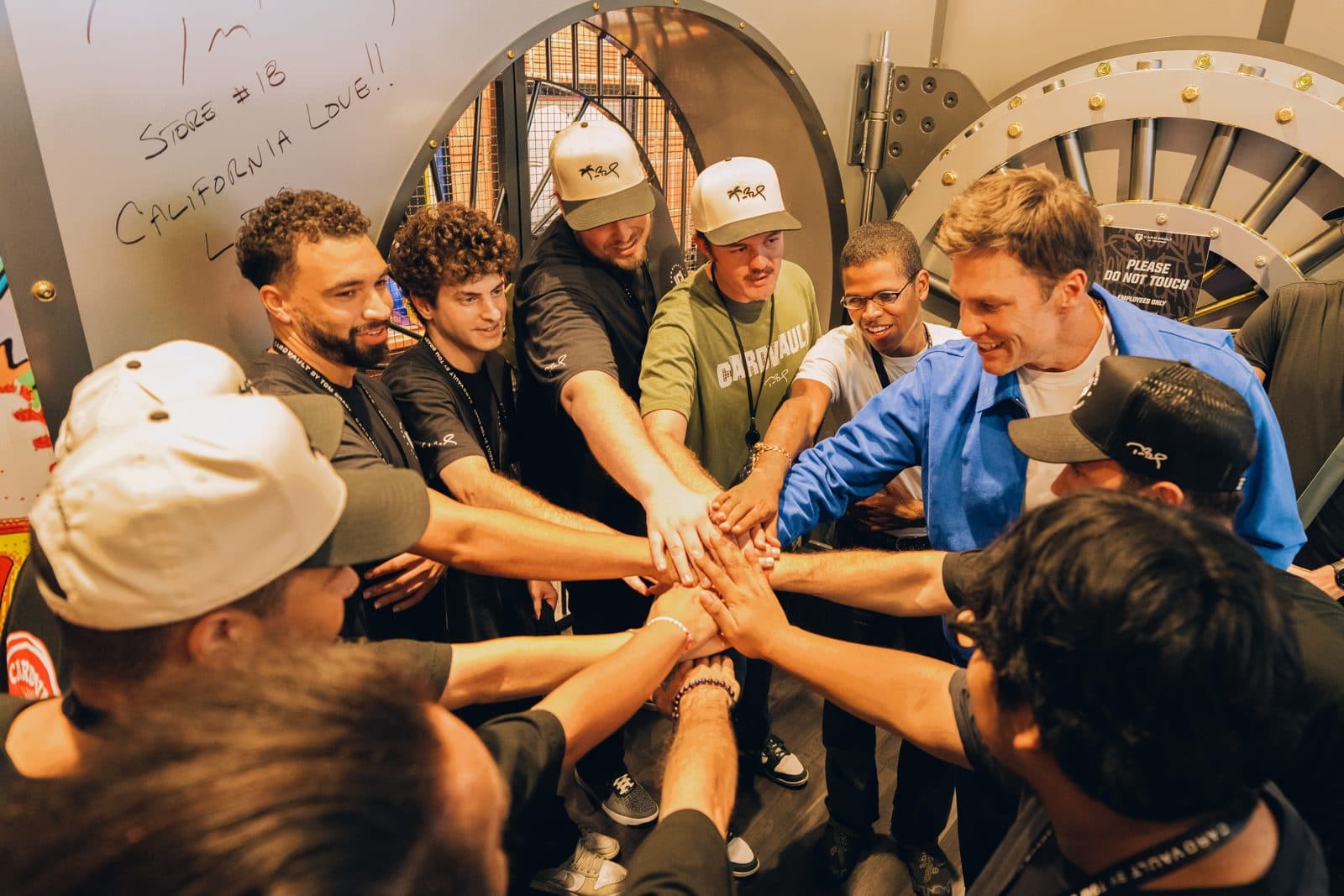 Tom Brady and the CardVault staff stack hands in a huddle in front of the vault door