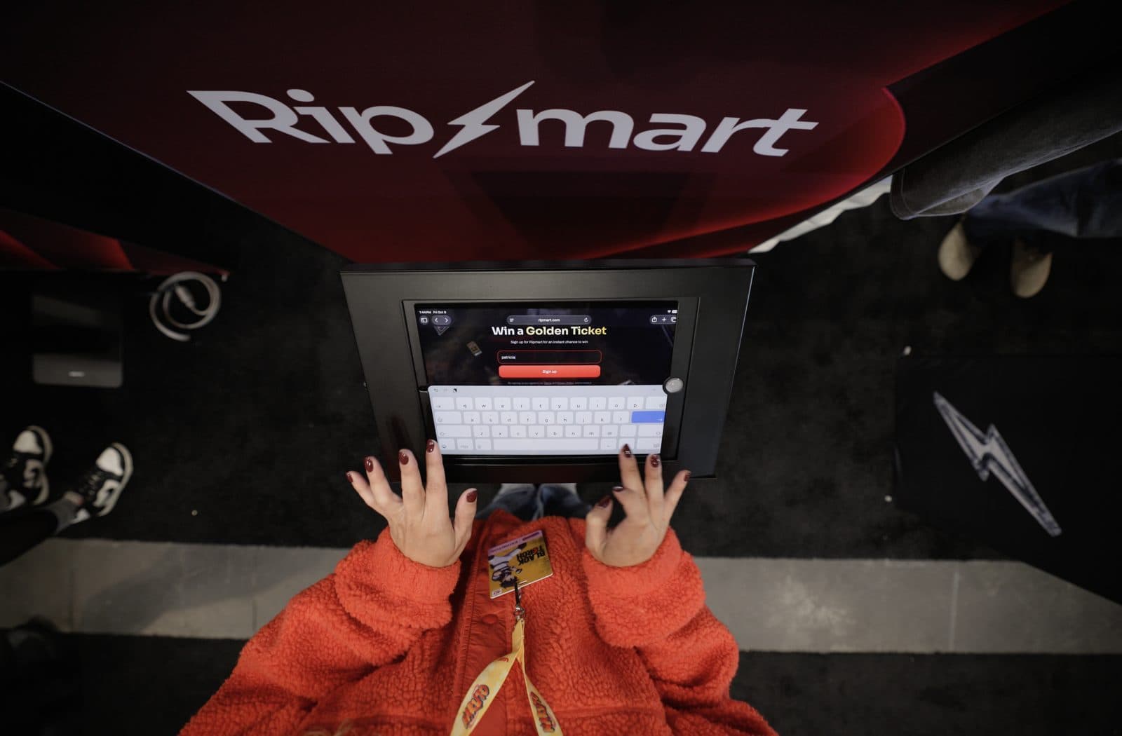 A visitor types on an iPad kiosk showing the Ripmart sign-up page headlined Win a Golden Ticket