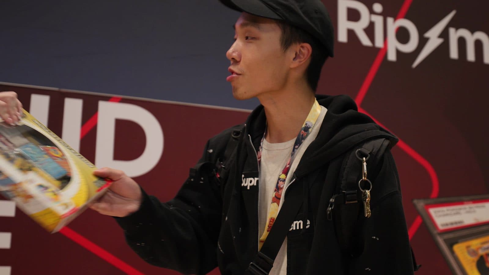A collector in a black cap is handed a sealed Pokémon box at the Ripmart booth