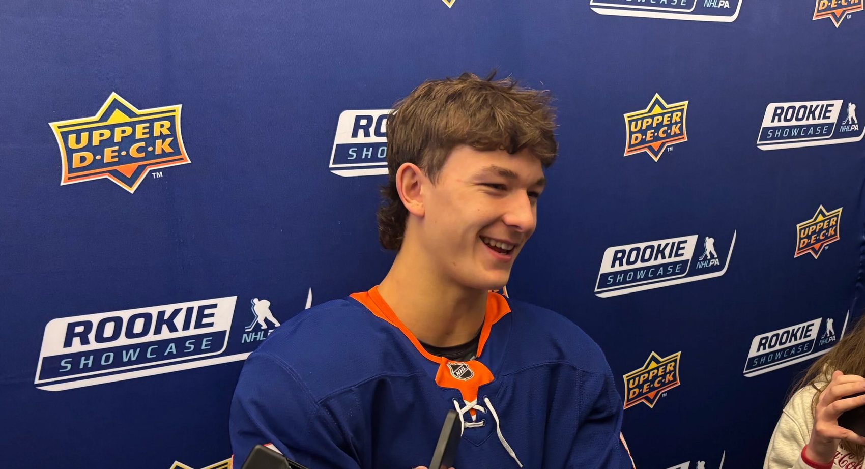 A rookie in a brand-new NHL jersey speaks to reporters in front of a backdrop repeating the Upper Deck and NHLPA Rookie Showcase logos